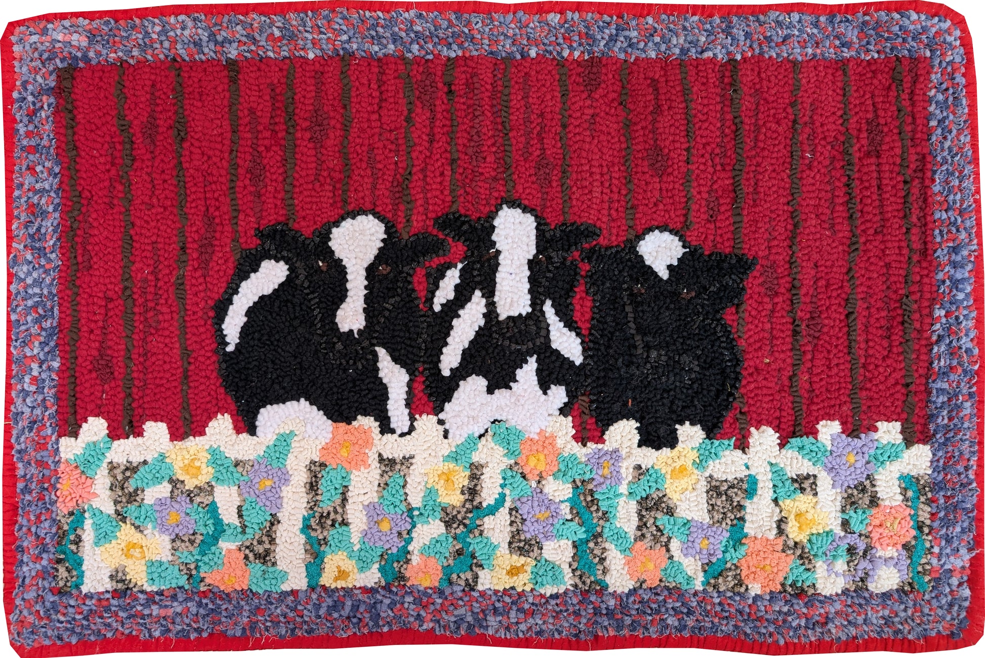 “Cow Klatch” – whimsical hand-hooked rug by Carmen Hall featuring black-and-white cows behind a floral fence on a red barn backdrop, outlined in dark green upholstery fabric.

